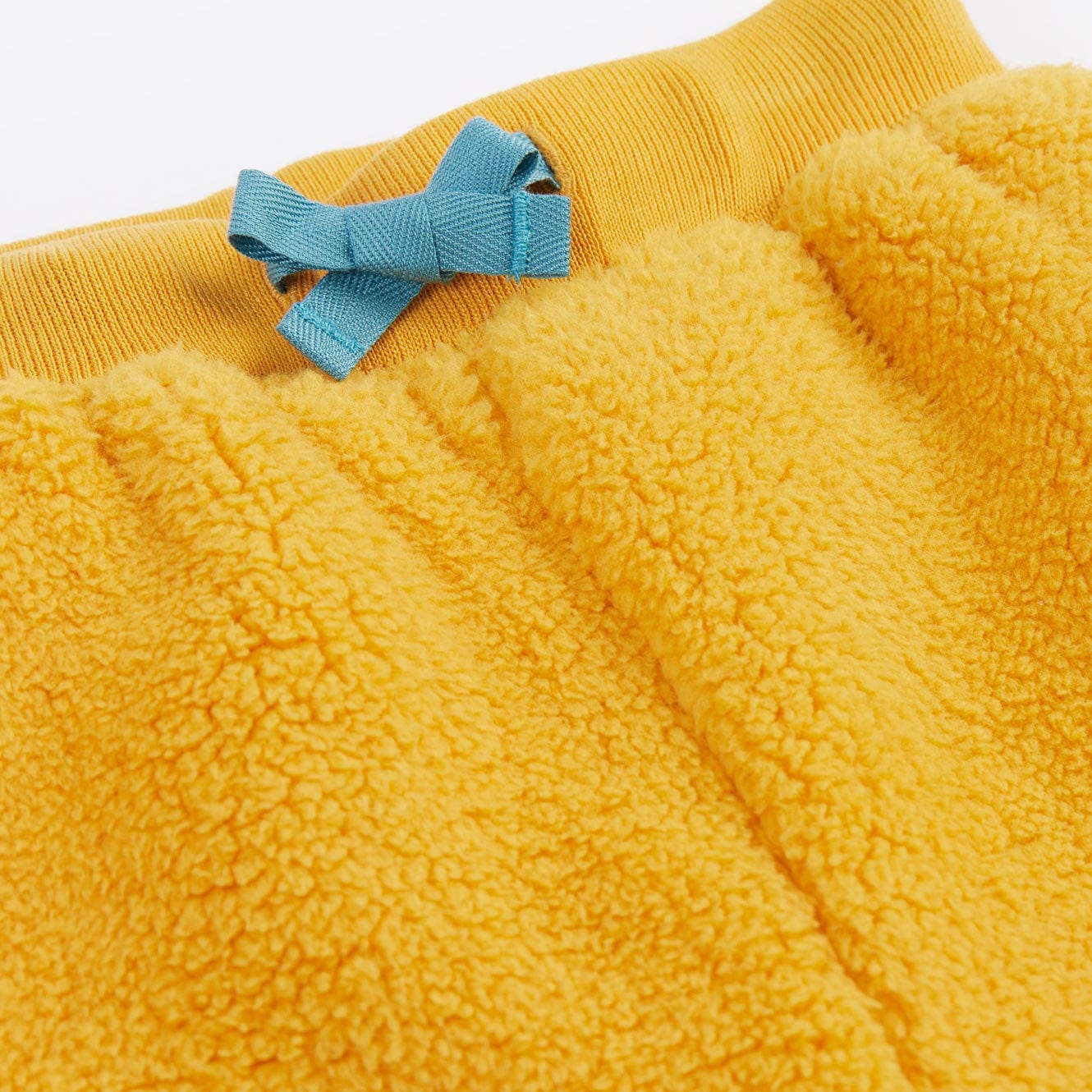 Close-up of a yellow fleece garment with a blue bow detail on a white background