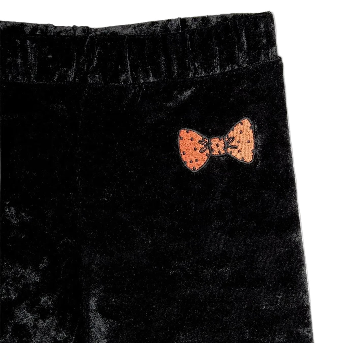 Close-up of black velvet pants with an orange bow-tie patch on the side, set against a plain white background.