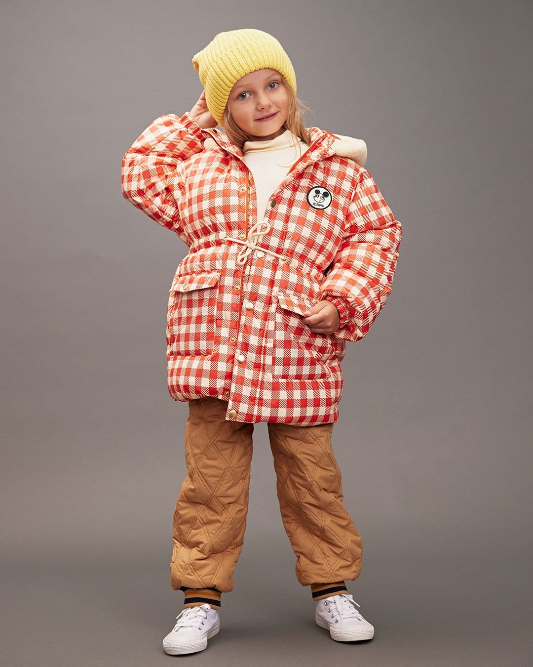 Child wearing a red checkered jacket and brown pants on a gray background