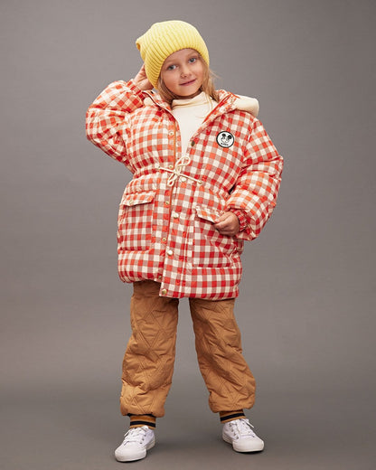 Child wearing a red checkered jacket and brown pants on a gray background