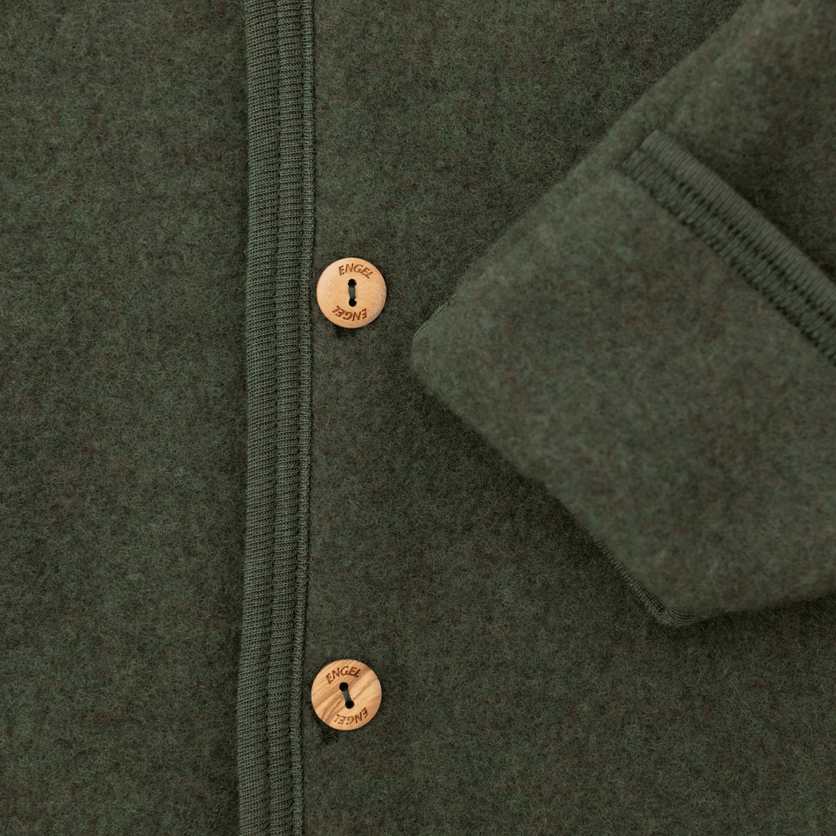 Close-up of a dark olive green wool jacket with a buttoned front and a folded cuff showing the ribbed lining.