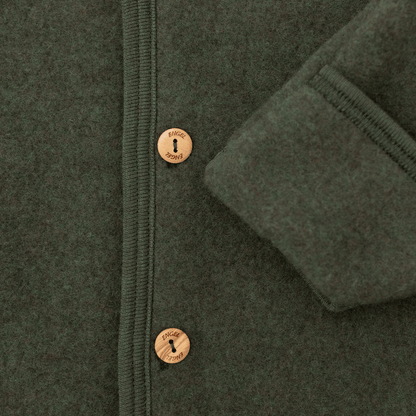 Close-up of a dark olive green wool jacket with a buttoned front and a folded cuff showing the ribbed lining.