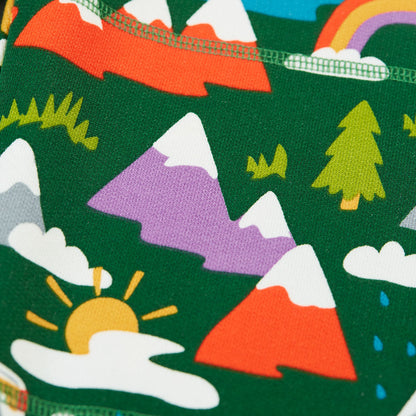 A close-up of a dark green fabric printed with a colorful children's landscape pattern featuring mountains, trees, clouds, a rainbow, and a sun.