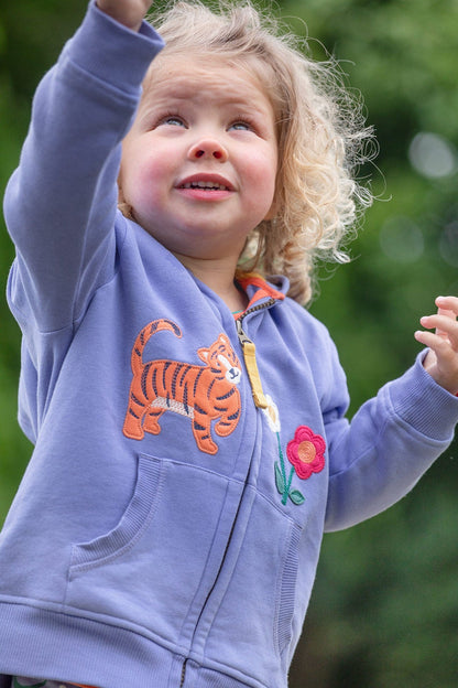 Blond toddler wearing Frugi's Carbis hoodie in purple with embroidered tiger and flowers at front.