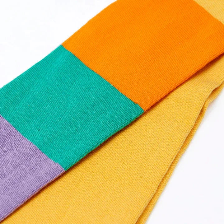 A close-up of a multi-colored striped knit sock with blocks of yellow, orange, teal green, and lavender purple on a white background.