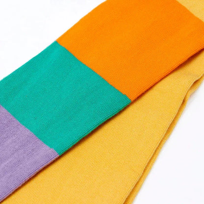 A close-up of a multi-colored striped knit sock with blocks of yellow, orange, teal green, and lavender purple on a white background.