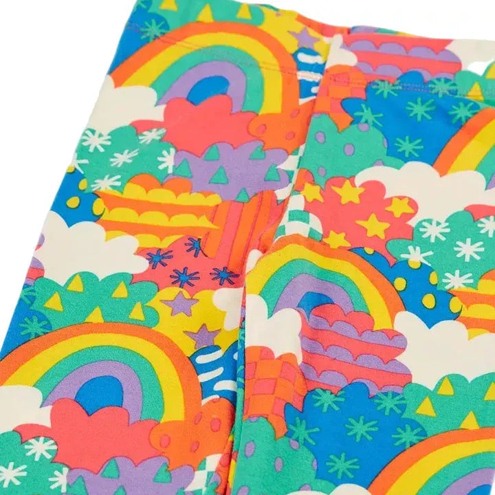A close-up of colorful children's leggings featuring a playful rainbow, cloud, and star pattern in bright blue, green, orange, pink, yellow, and purple.