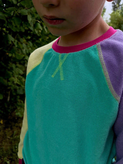 Close-up of a child wearing a colorful sweater with a green design against a blurred natural background